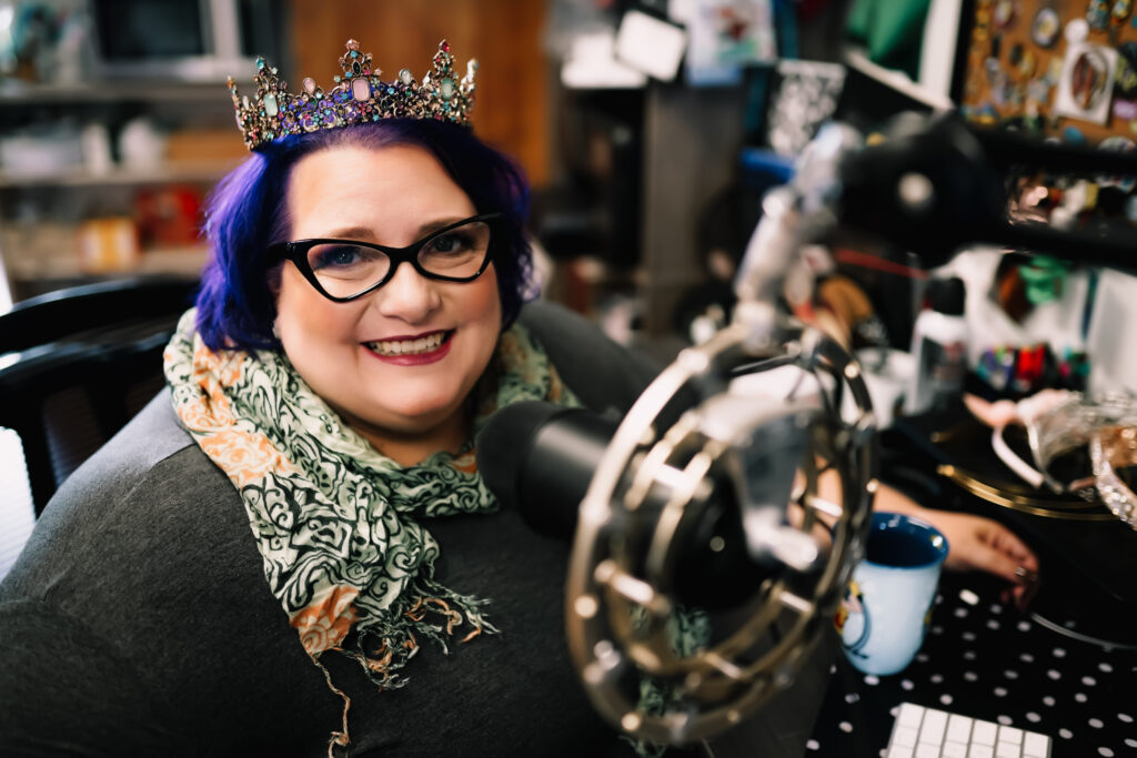 Michelle sitting at her desk with a podcasting mic on a boom and a tiara on her head.