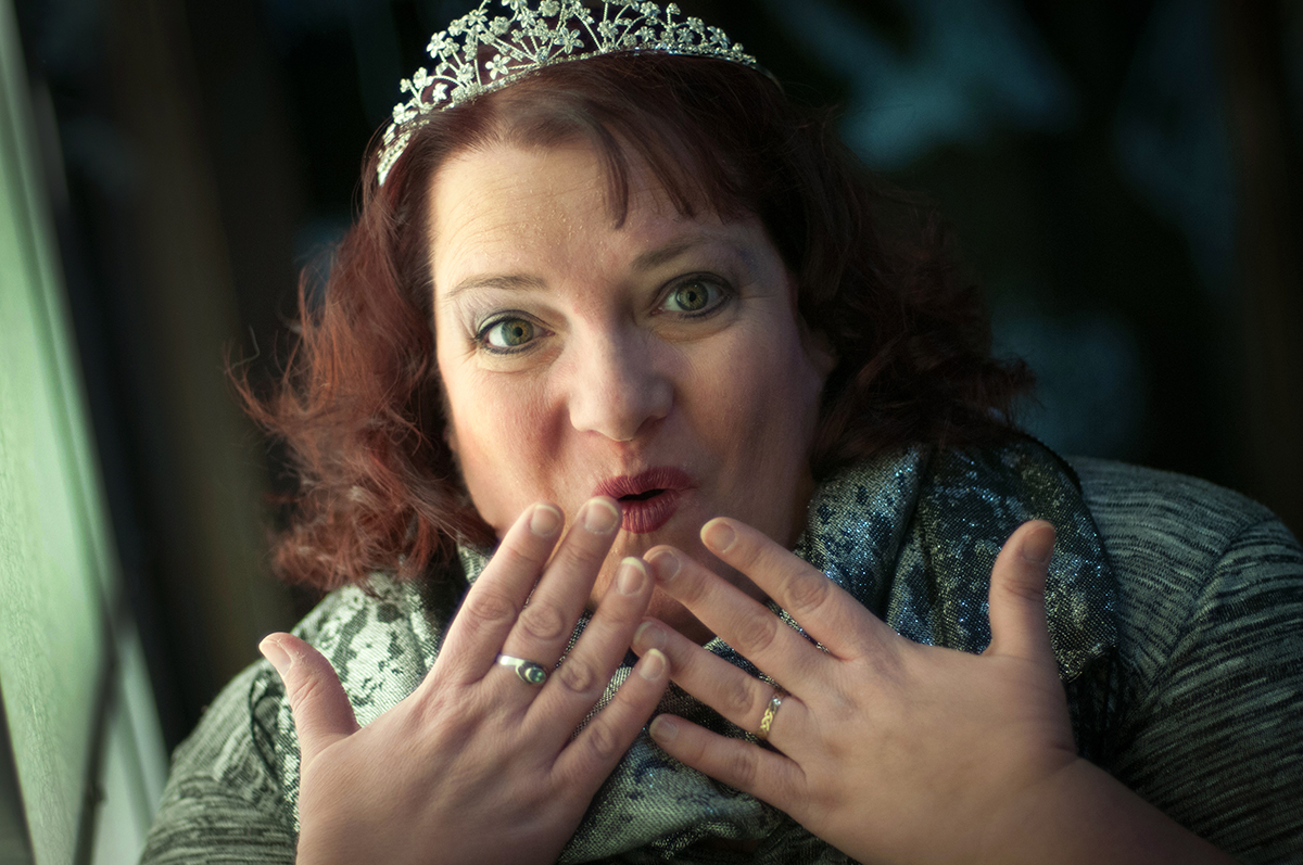 Michelle in a tiara with a surprised face and her hands up.