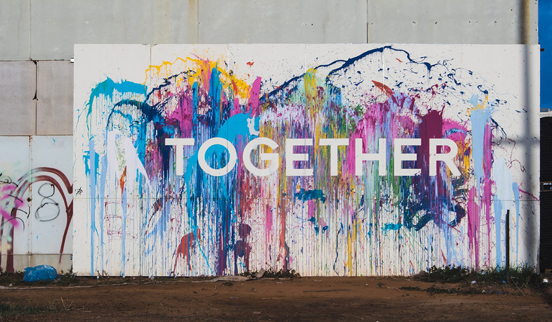 A wall with lots of different colored paint splashed on it with the word "Together"