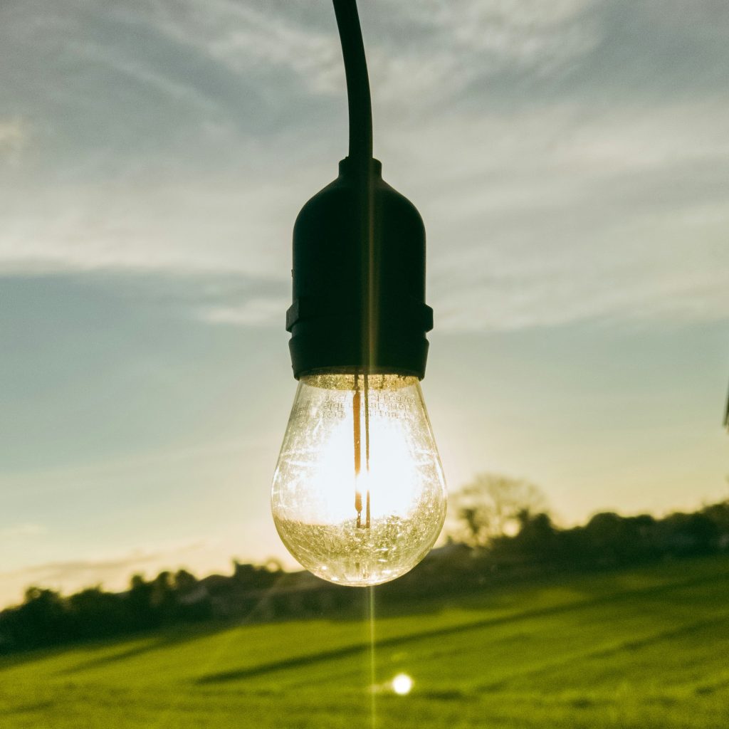 A glowing lightbulb hanging with a landscape of an expansive meadow in the background